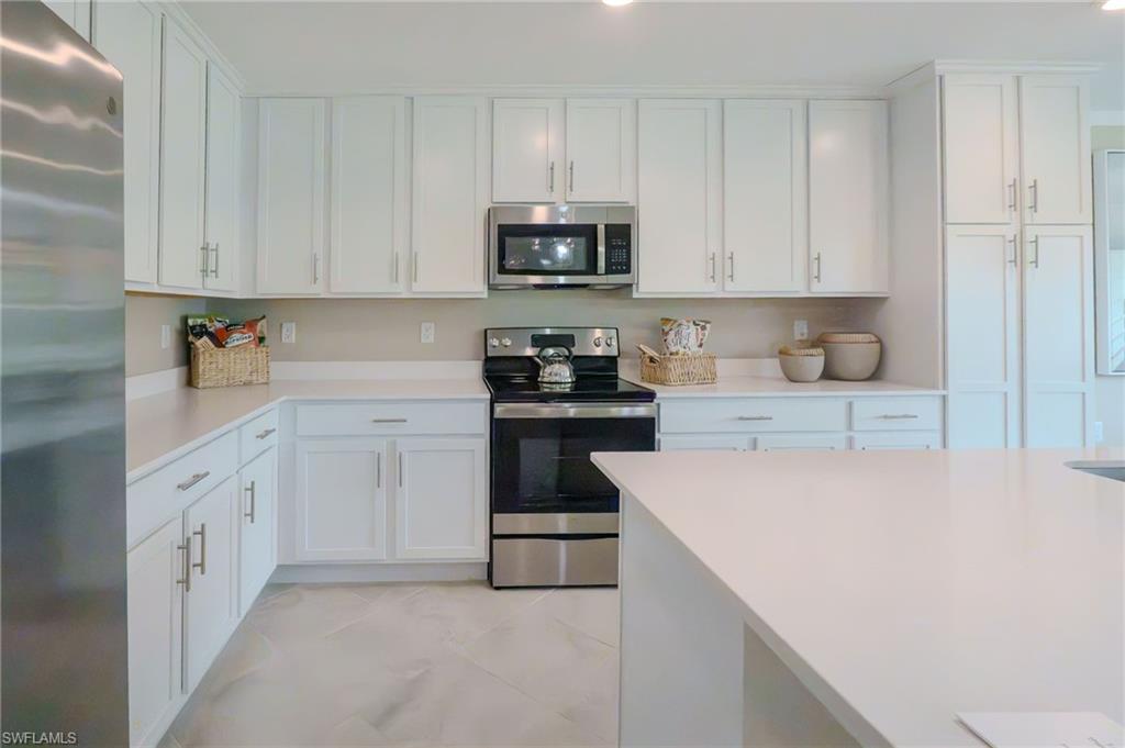 White cabinetry with silver-tone hardware, stainless steel appliances, light-toned countertops, and large format floor tiling