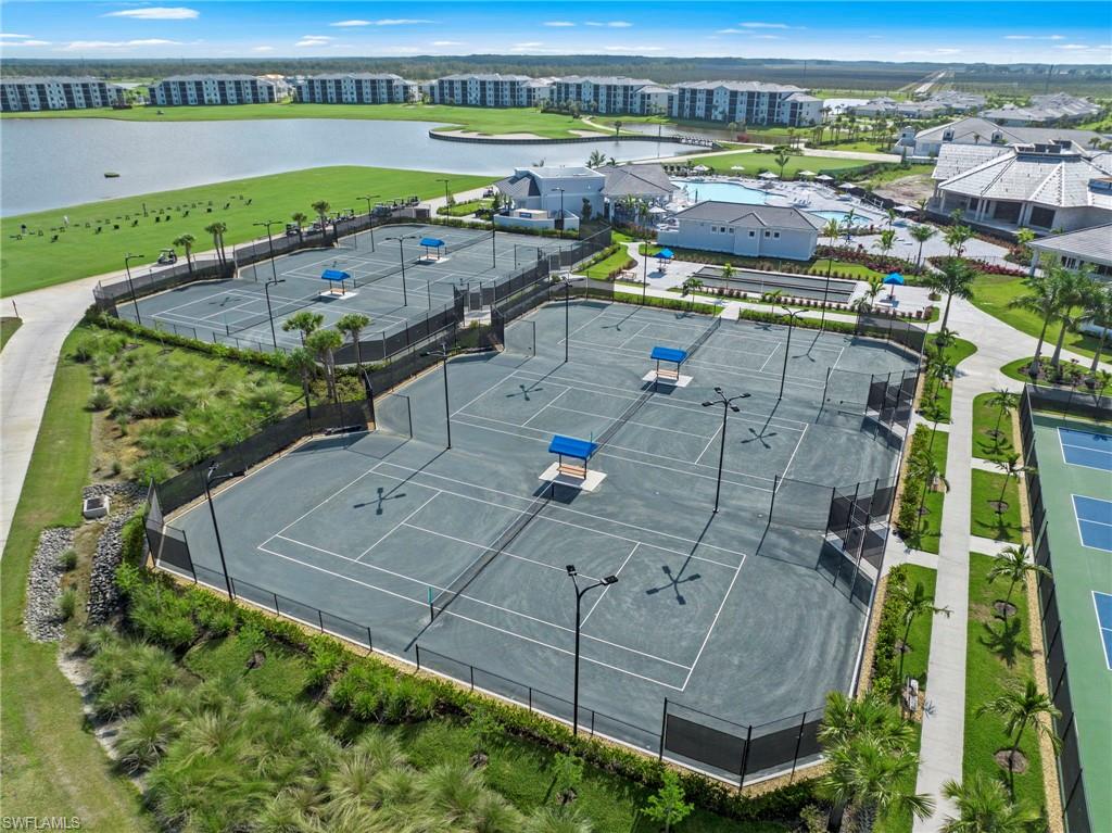 Multiple tennis courts with dark gray surfaces, integrated lighting, and blue shaded benches