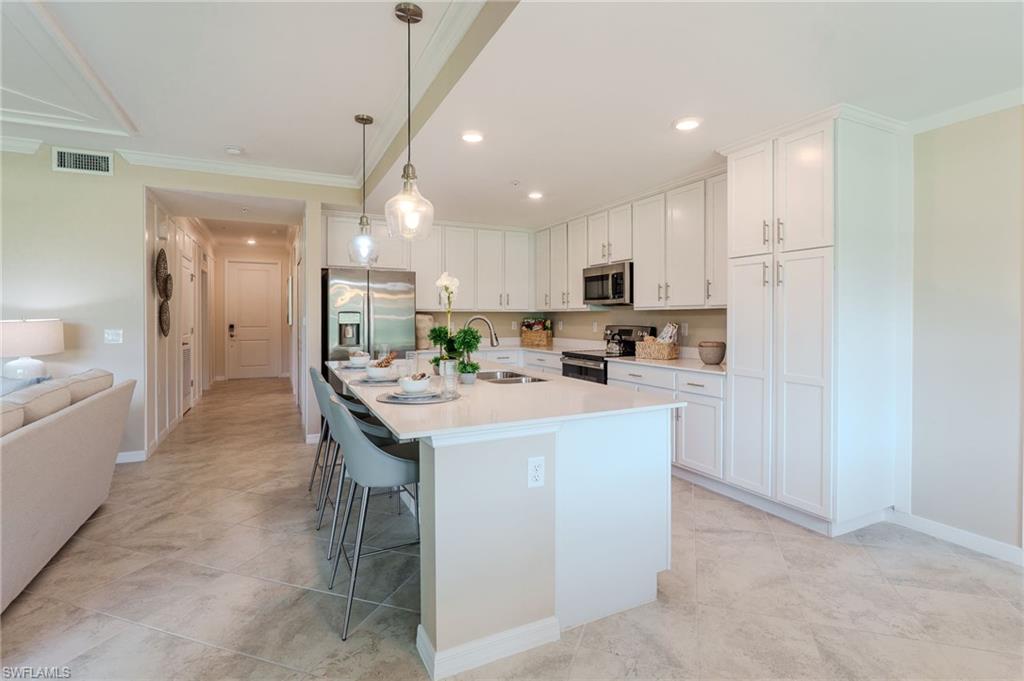 Spacious kitchen featuring white cabinetry, a large island with counter seating, stainless steel appliances, and pendant lighting