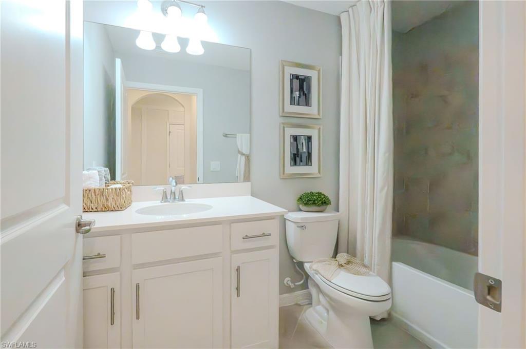 Bathroom featuring a white vanity with a single sink, an integrated mirror with overhead lighting, a toilet, and a shower-tub combination
