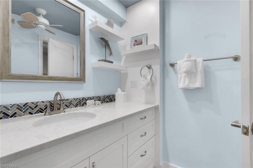 White vanity with brushed nickel hardware, countertop with integrated sink, herringbone tile backsplash, and wall-mounted mirror