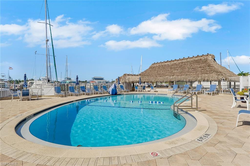 Oval-shaped swimming pool with a stone paver surround, stainless steel grab rails, and a thatched-roof cabana