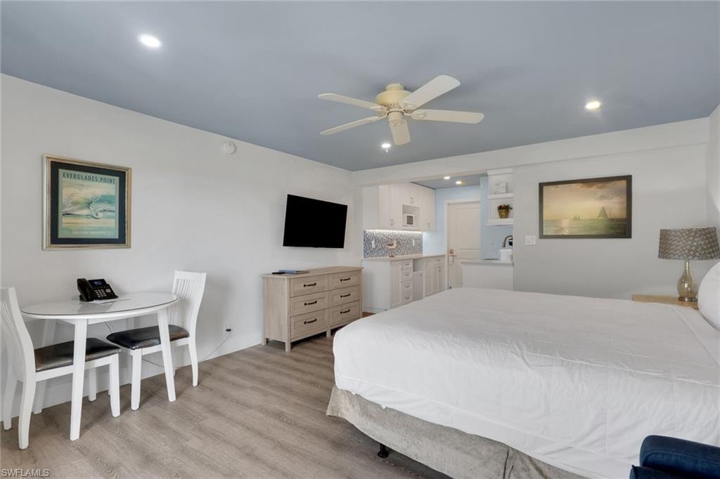 Recessed lighting, wood-finish flooring, ceiling fan, and a kitchenette with white cabinetry and a patterned tile backsplash