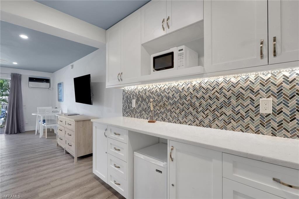 White cabinetry with brushed nickel hardware and a microwave, quartz countertop, and mosaic tile backsplash