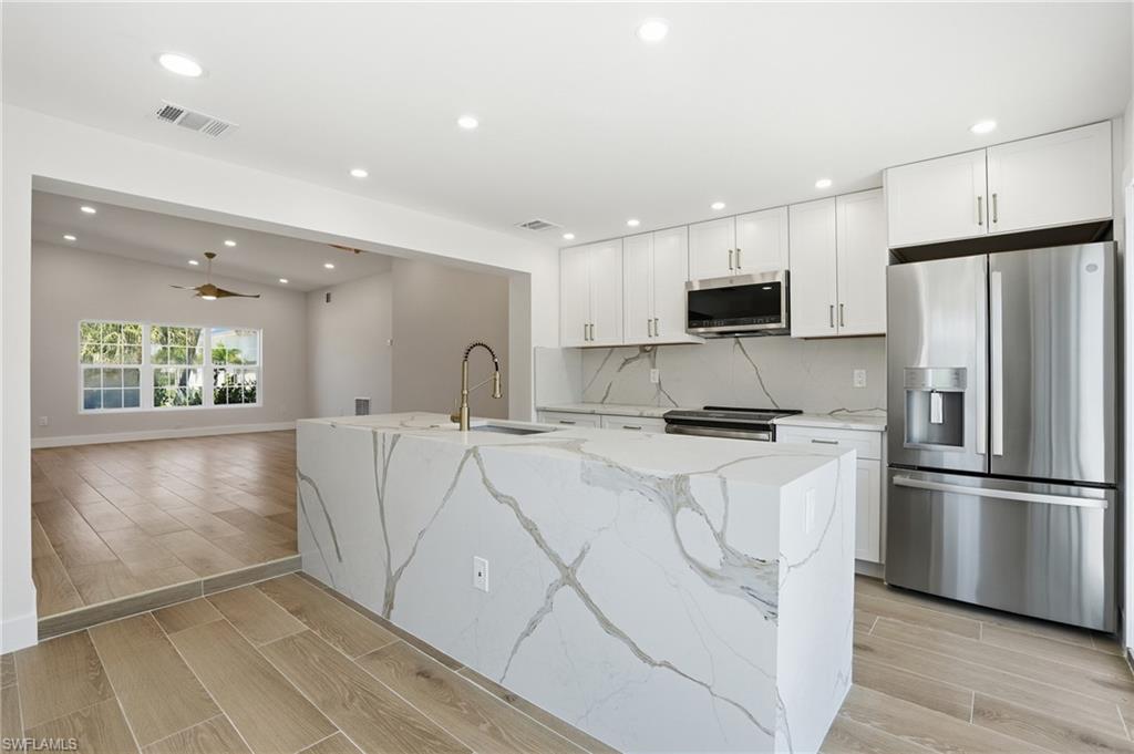 The kitchen features a large island with a waterfall edge and integrated sink, stainless steel appliances, and white cabinetry - Virtually Edited Image