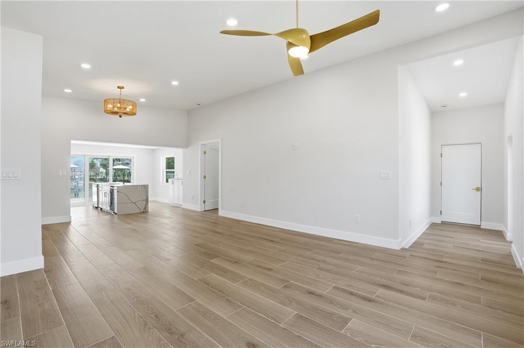 Spacious living area featuring light wood-look flooring, recessed lighting, and a modern ceiling fan - Virtually Edited Image