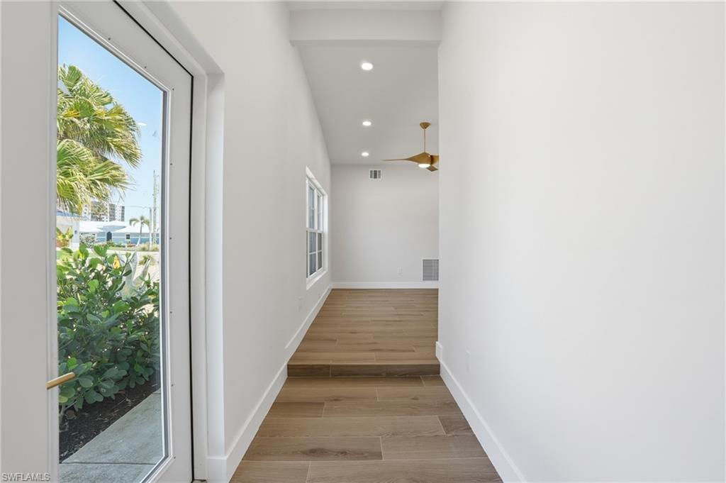 Inviting entry with light-toned flooring, crisp white walls, and a large glass-paned door offering natural light and views of tropical foliage - Virtually Edited Image