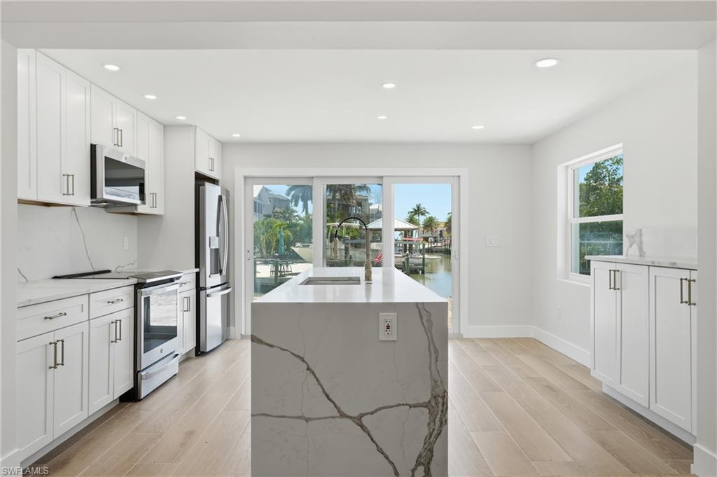 Modern kitchen with light wood flooring, white cabinetry, stainless steel appliances, and a central island featuring a waterfall countertop - Virtually Edited Image
