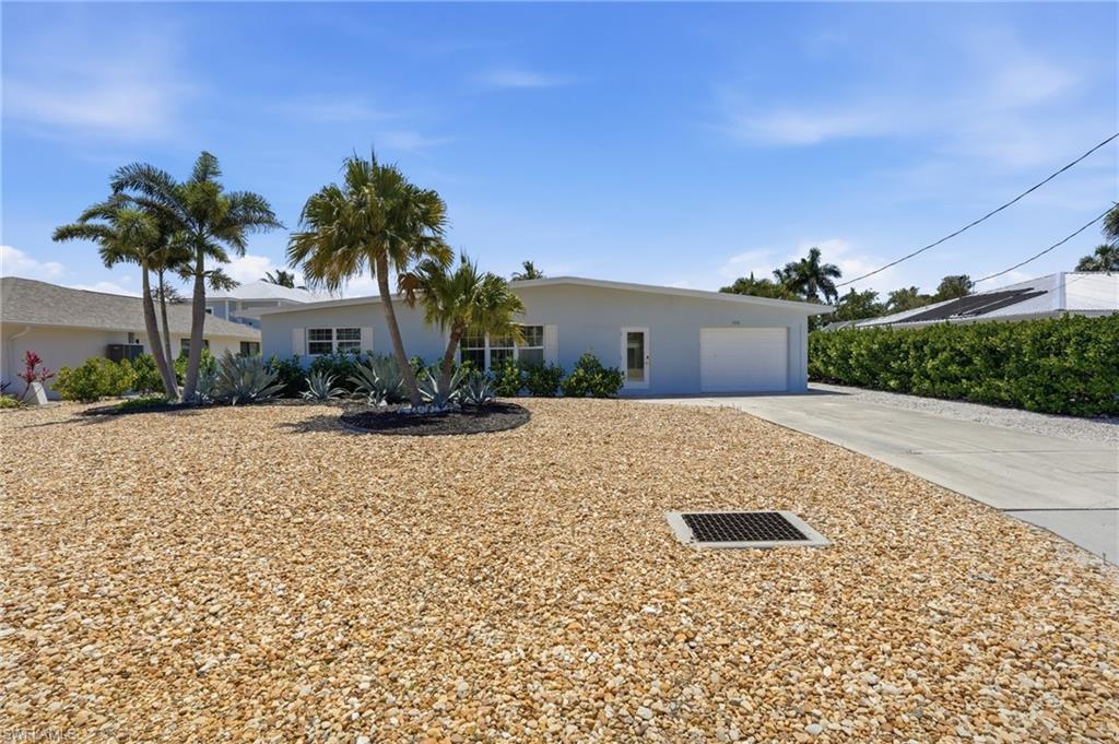 The property features a light-colored exterior with a white garage door, a concrete driveway, and a gravel-covered yard - Virtually Edited Image