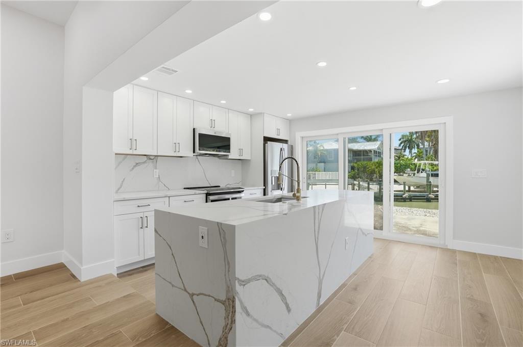 Modern kitchen featuring light wood-style flooring, white cabinetry, a large kitchen island, and a stainless steel refrigerator - Virtually Edited Image