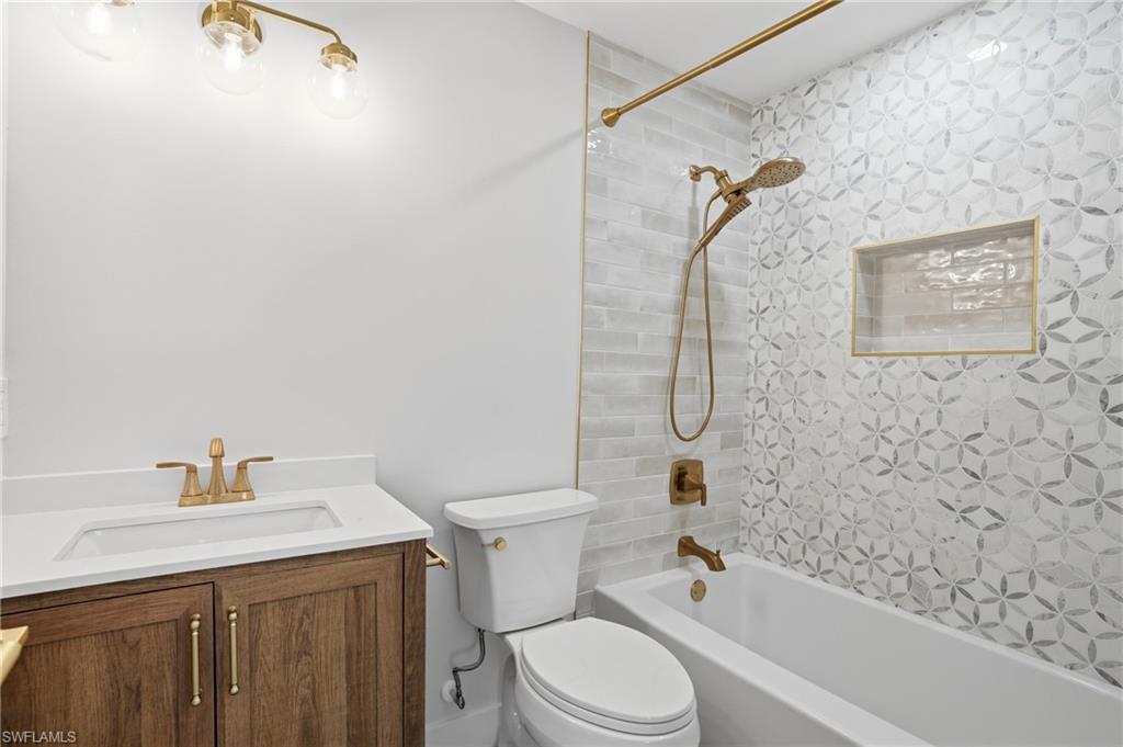 Bathroom featuring a vanity with a white countertop and wood cabinetry, a white toilet, and a white bathtub with a tiled surround - Virtually Edited Image