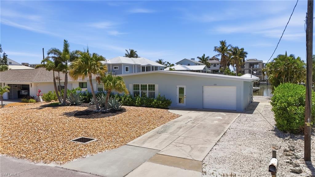 The property features a concrete driveway leading to a garage, a gravel yard with mature palm trees, and views of a canal - Virtually Edited Image