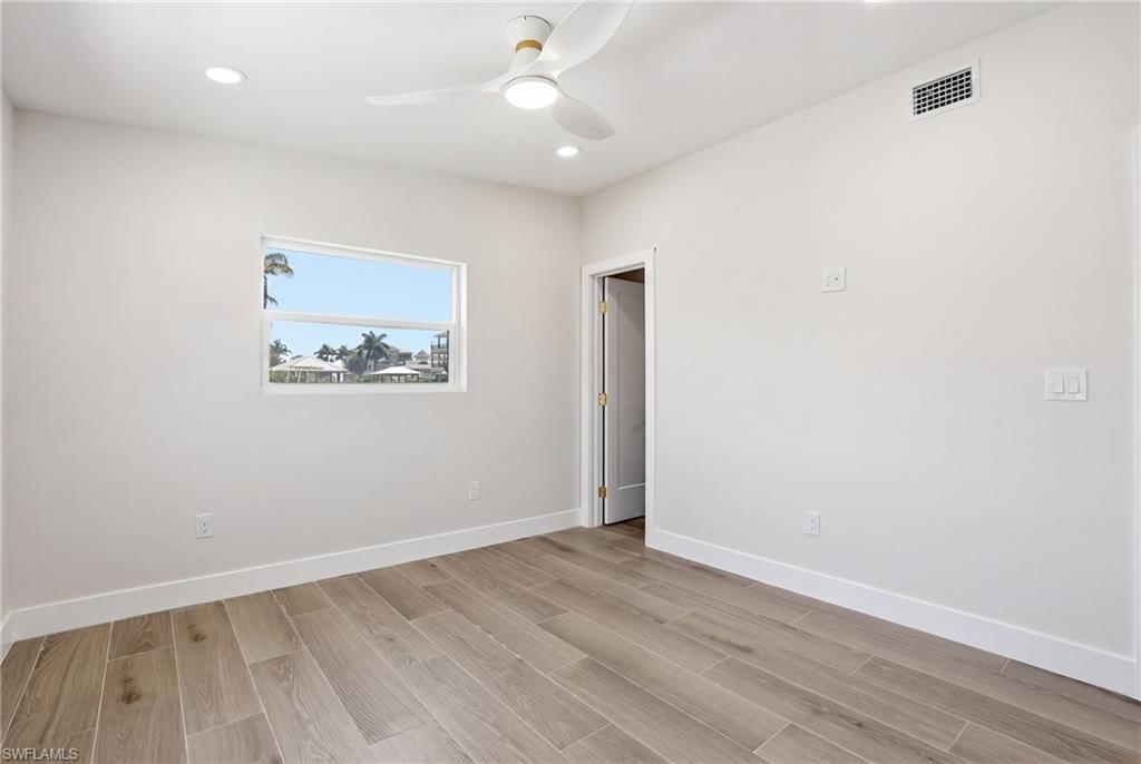 This room features light wood-look flooring, a window with a water view, and a ceiling fan with integrated lighting - Virtually Edited Image