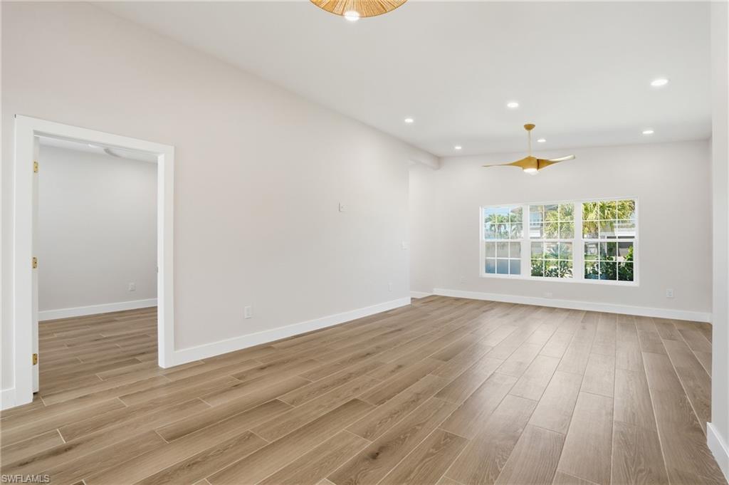Spacious room featuring light wood-style flooring, white walls, and a contemporary ceiling fan - Virtually Edited Image