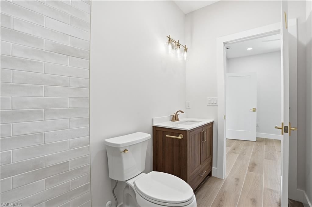 The bathroom features a toilet with a brass flush lever, a vanity with a dark wood cabinet and white countertop, and a brass faucet - Virtually Edited Image