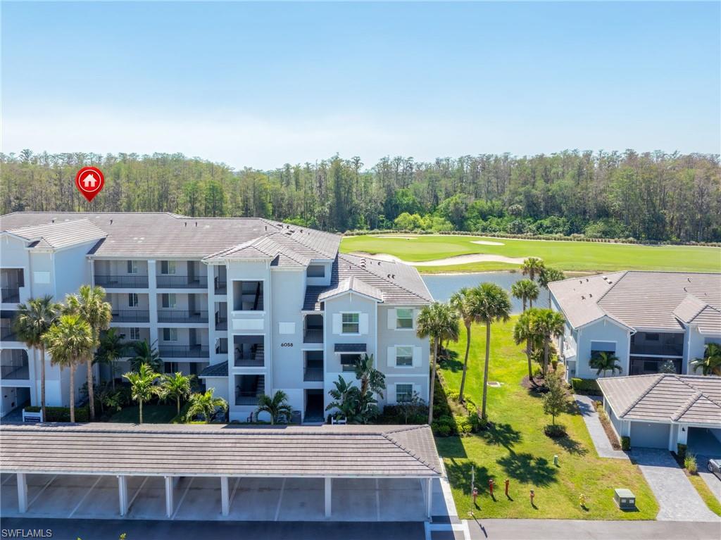 Multi-story residential structure with a covered parking area, golf course frontage, water features, and mature palm trees