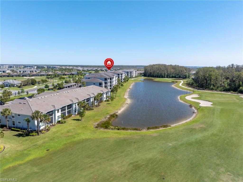 Expansive golf course frontage with a pond, surrounding residential buildings, and a distant tree line