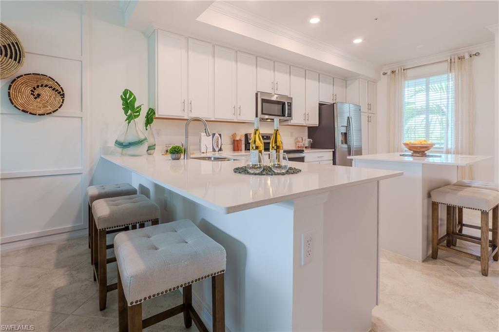 Bright kitchen featuring white cabinetry, a large kitchen island with counter seating, stainless steel appliances, and a window with natural light