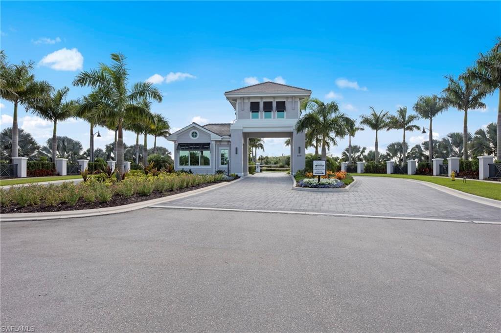 Decorative entrance gatehouse with paved driveway and lush landscaping, featuring palm trees and a low-profile boundary wall