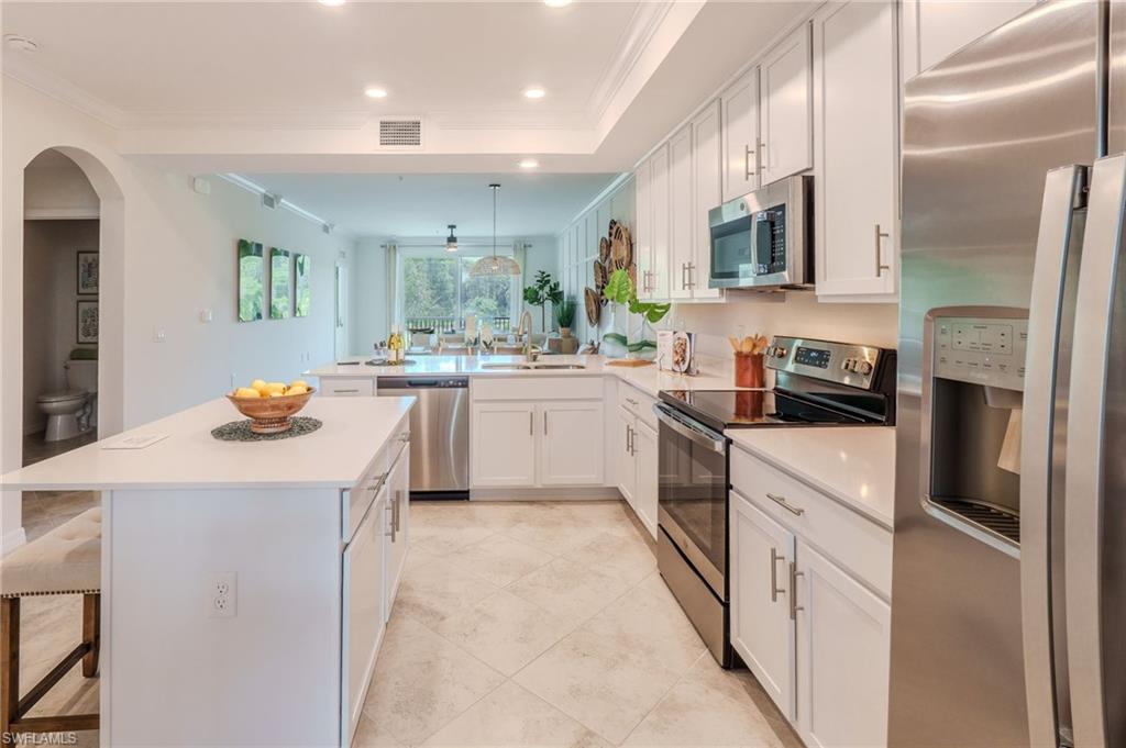 White shaker cabinetry, stainless steel appliances, recessed lighting, expansive kitchen island, and light-toned tile flooring