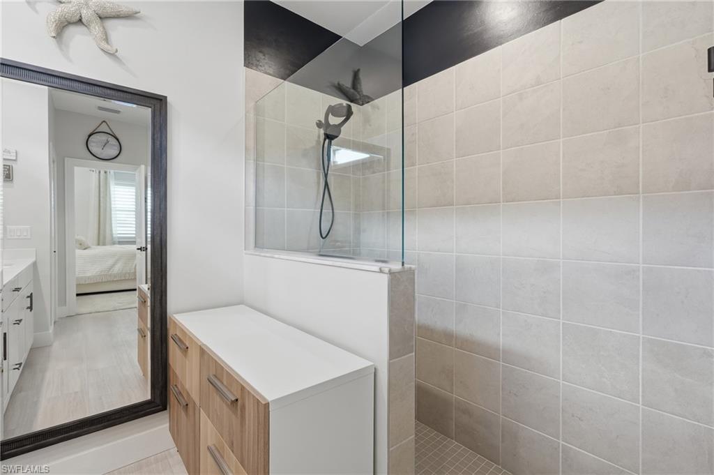 Modern primary bathroom featuring a frameless glass shower enclosure with chrome fixtures, a floating wood-finish vanity with white quartz countertop, neutral tile walls, and polished concrete flooring throughout