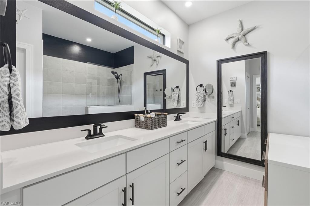 Spa-inspired primary bathroom featuring dual vanities with white cabinetry, quartz countertops, and matte black hardware