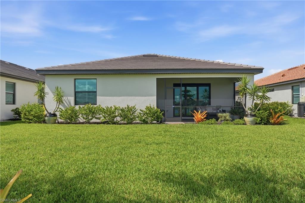 Contemporary home with clean architectural lines and a modern aesthetic, featuring a wide front-facing porch with glass sliding doors, large windows with dark frames, and a manicured lawn bordered by tropical landscaping including palms and flowering plants
