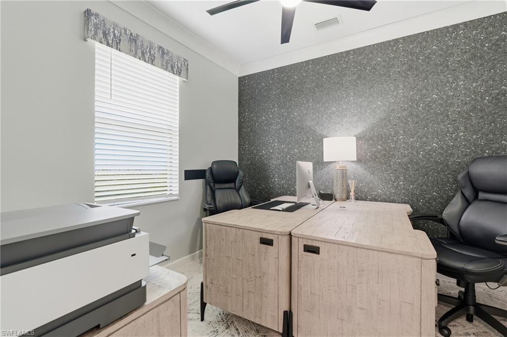 Professional home office featuring textured accent wallpaper, dual wood-finish desks with integrated storage, black ergonomic task seating, recessed ceiling lighting, and horizontal window blinds with coordinating valance