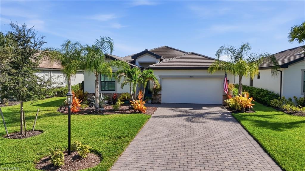 Striking single-story residence featuring a professional brick paver driveway, manicured landscaping with mature palms and tropical plantings, and a three-car garage