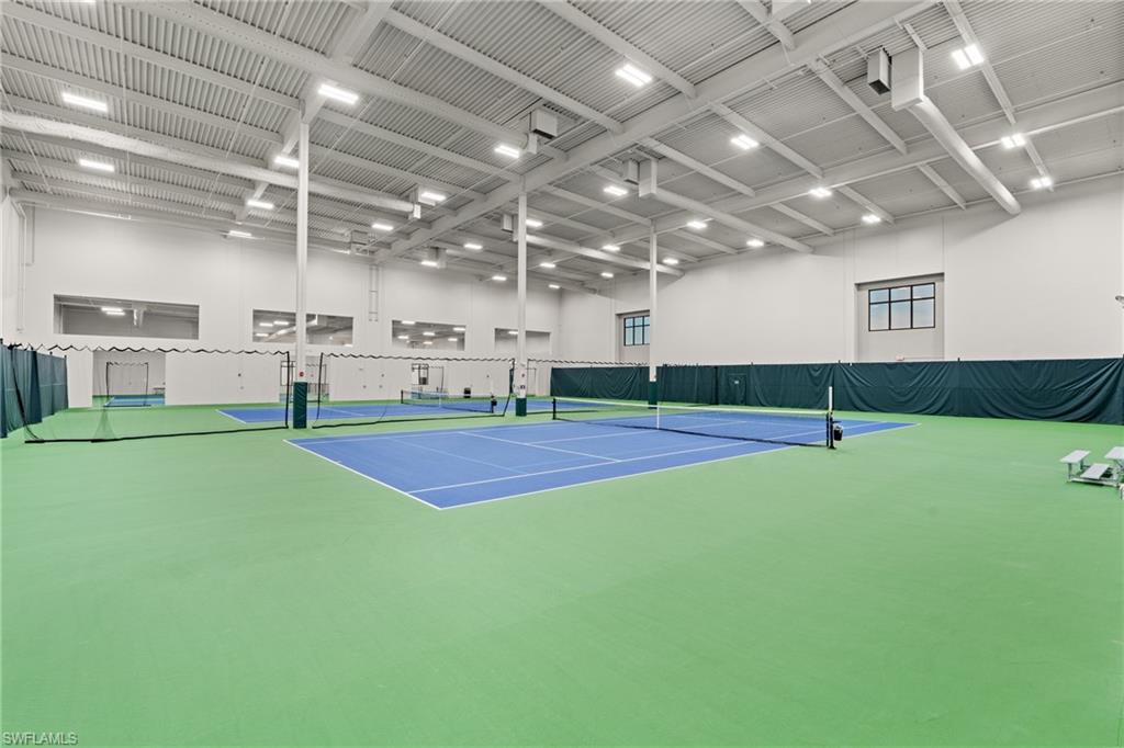 State-of-the-art indoor tennis facility featuring multiple courts with professional-grade hard courts in contrasting blue and green surfaces, regulation net systems, and soaring ceilings with integrated LED lighting throughout