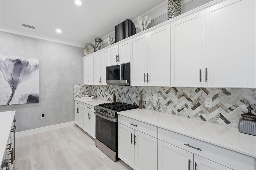 Sleek galley kitchen featuring white cabinetry with brushed metal hardware, quartz countertops, a geometric marble tile backsplash, stainless steel gas range, and built-in microwave