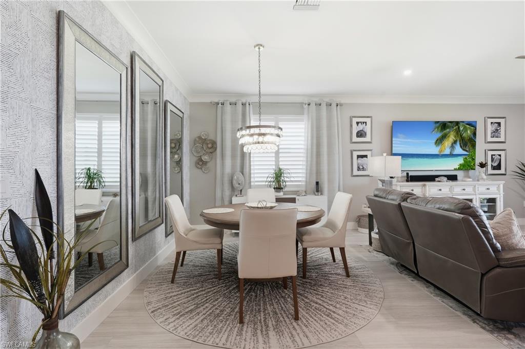 Open-concept living space featuring a round pedestal dining table, neutral upholstered seating, light wood-finish flooring, and a circular area rug anchoring the dining zone