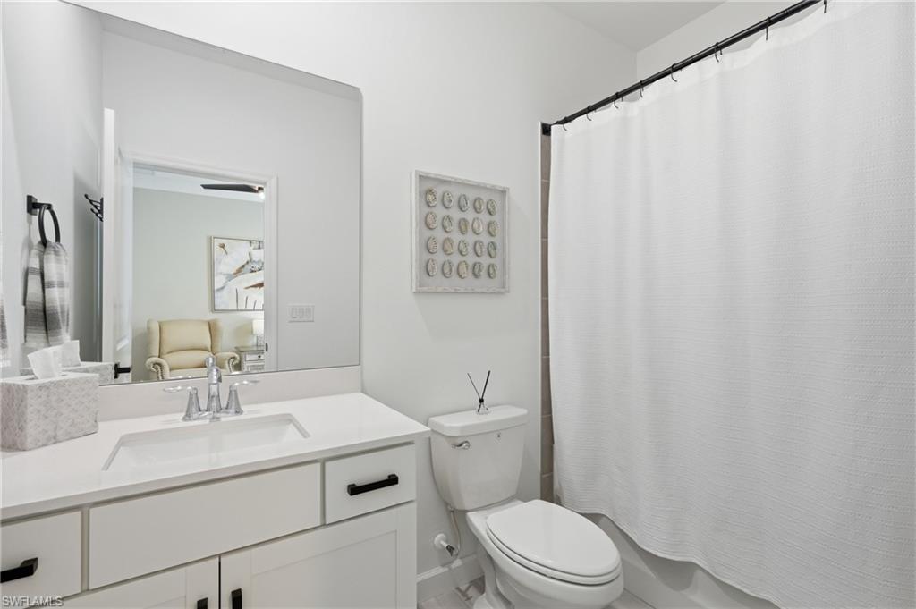 Modern bathroom featuring a white vanity with dual drawers and black hardware, white quartz countertop, chrome faucet, large illuminated mirror, white subway tile surround, and a separate toilet with white shower curtain enclosure