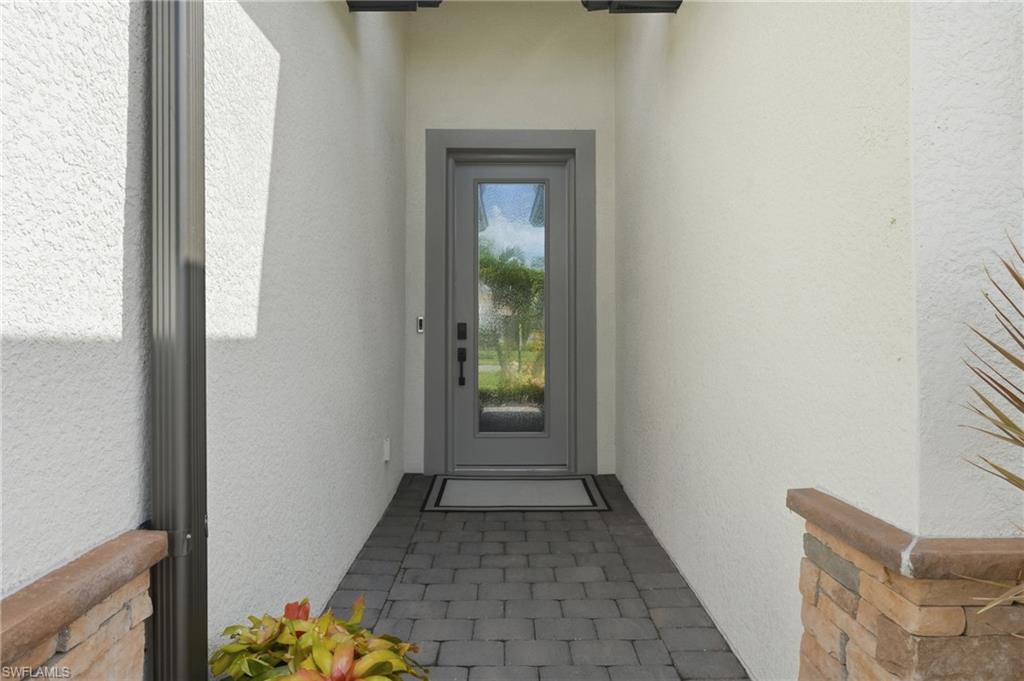 Modern entryway featuring a narrow tile-paved corridor with charcoal-gray framed glass door, white textured walls, and warm wood-finish trim accents
