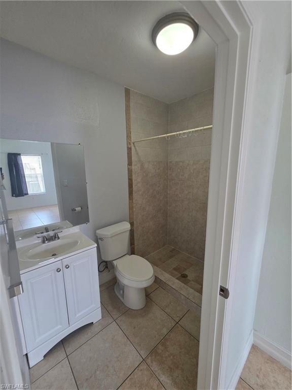 Bathroom featuring a white vanity with a single basin, a toilet, a tiled shower, and neutral-toned floor tile