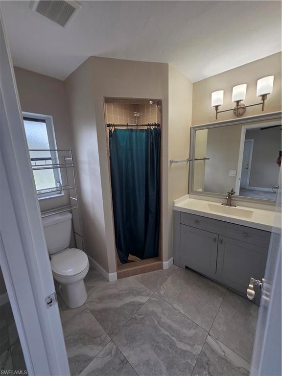 Gray tile flooring set on a diagonal, shower stall with tiled walls, vanity with gray cabinetry and integrated sink, wall-mounted mirror, and a three-light vanity fixture