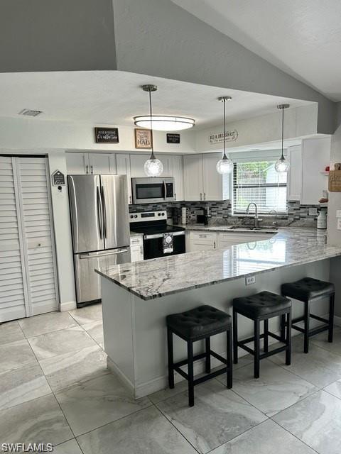 Kitchen featuring stainless steel appliances, white cabinetry, a large kitchen island with counter seating, pendant lighting, and tile flooring