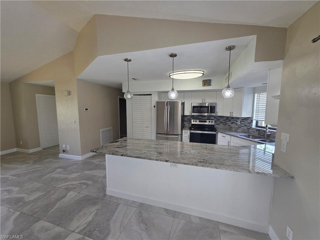 Kitchen featuring light-toned cabinetry, stainless steel appliances, a tiled backsplash, and a breakfast bar with a stone countertop