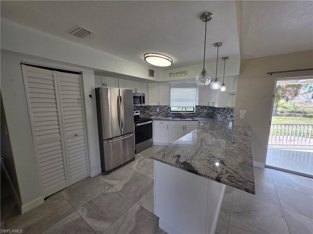 White cabinetry, stainless steel appliances, patterned backsplash, granite countertop with breakfast bar, and tile flooring