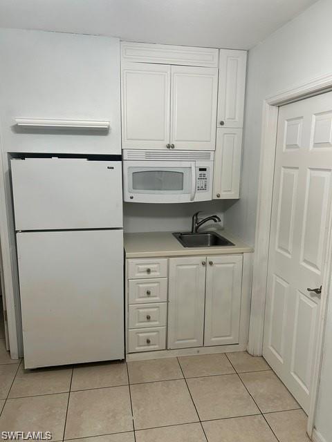 Compact kitchenette featuring white cabinetry, a stainless steel microwave, tile flooring, a single-basin sink with faucet, and a top-freezer refrigerator
