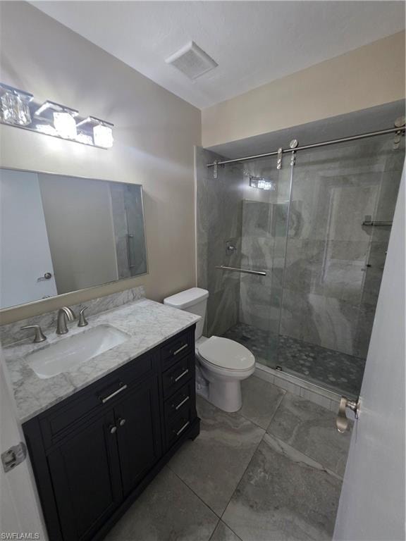 Vanity with a marble-style countertop and undermount sink, brushed nickel faucet, dark wood-finish cabinetry, and a glass-enclosed shower with tiled walls and a pebble-style floor