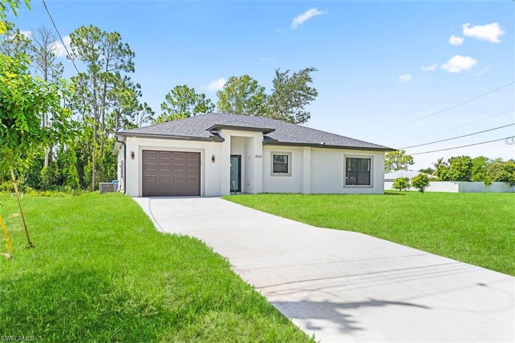 Modern residence featuring a clean architectural design with a light-toned exterior, attached garage with paneled door, concrete driveway, expansive manicured lawn, and mature landscaping with established trees throughout the grounds