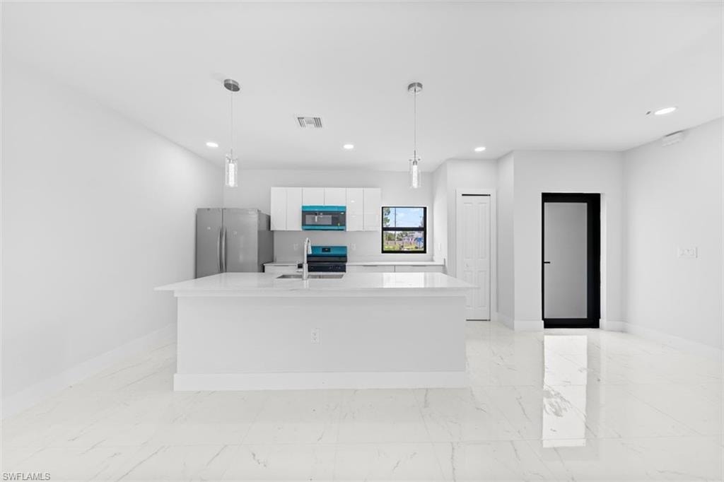 Kitchen featuring a large island with a sink, white cabinetry, stainless steel appliances, and pendant lighting