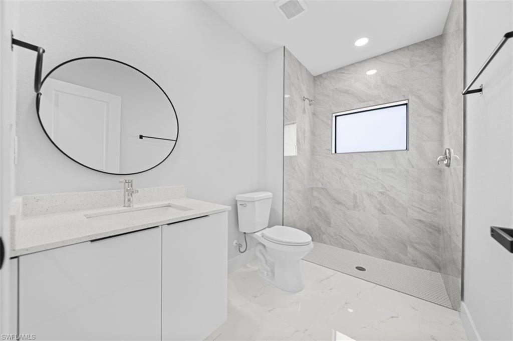 Modern bathroom featuring a single vanity with a white countertop, circular mirror, and a walk-in shower with tiled walls