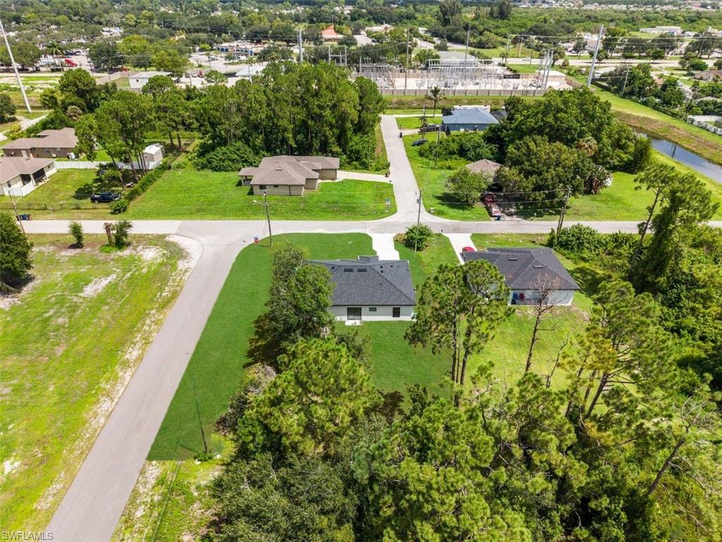 Aerial perspective featuring two properties with dark shingle roofs, manicured lawns, and mature trees