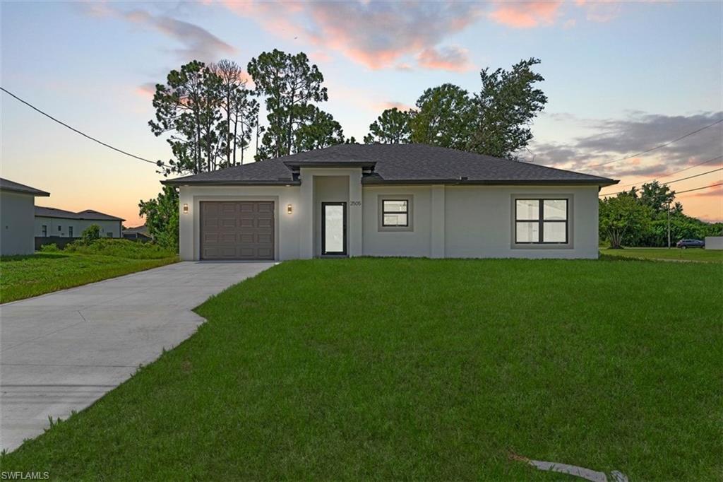 Modern single-story exterior with a dark shingle roof, attached garage, concrete driveway, and a manicured lawn