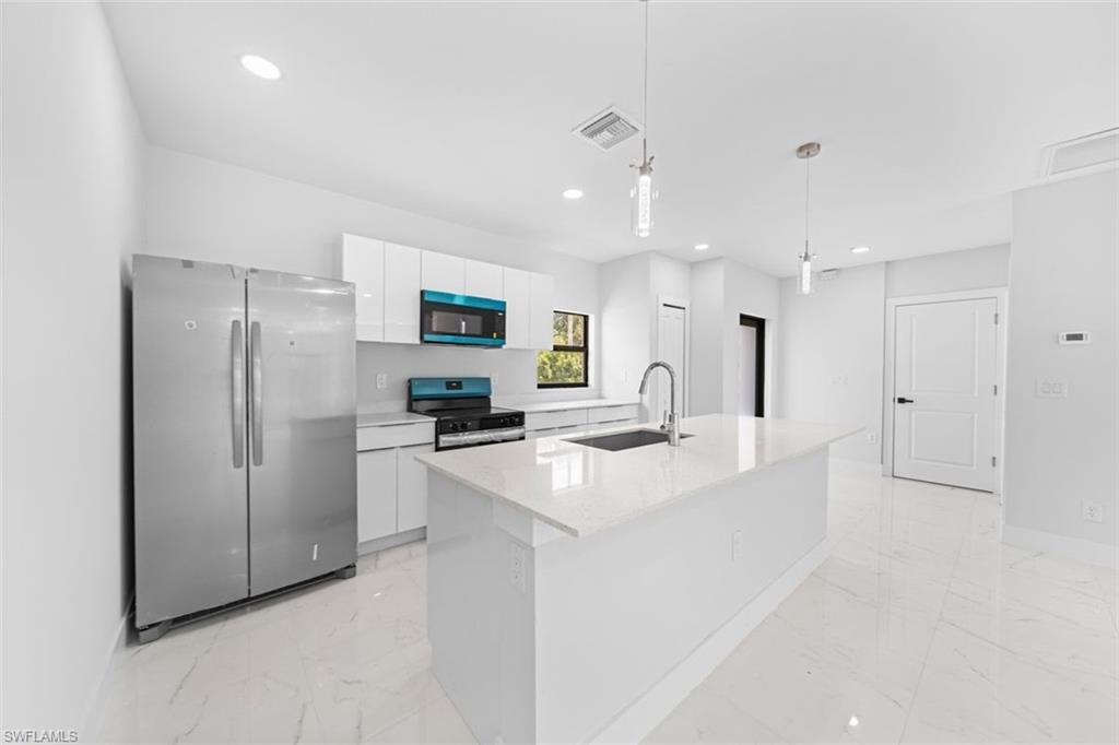 Contemporary kitchen featuring stainless steel side-by-side refrigerator, white cabinetry with integrated hardware, quartz waterfall island countertop, stainless steel sink with gooseneck faucet, and built-in stainless steel appliances