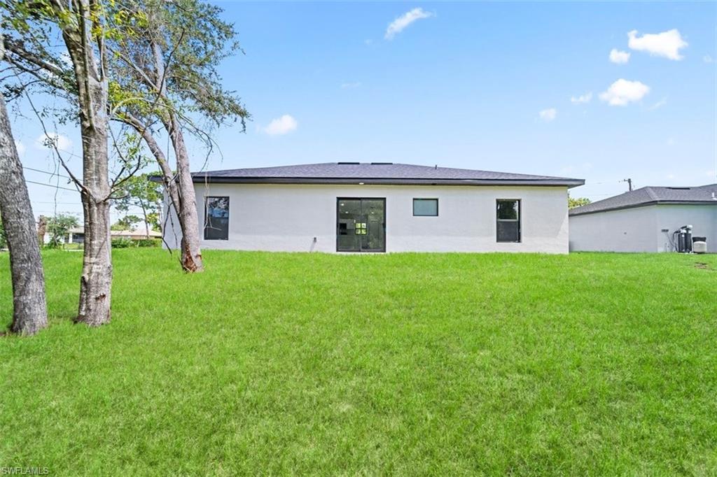 Expansive green lawn with mature trees, a light-colored exterior, and dark-framed windows