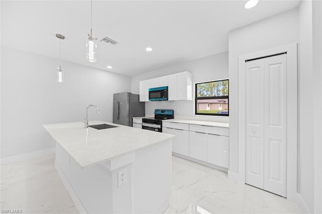 Kitchen featuring a white countertop island, stainless steel sink, modern pendant lighting, white cabinetry, and stainless steel appliances
