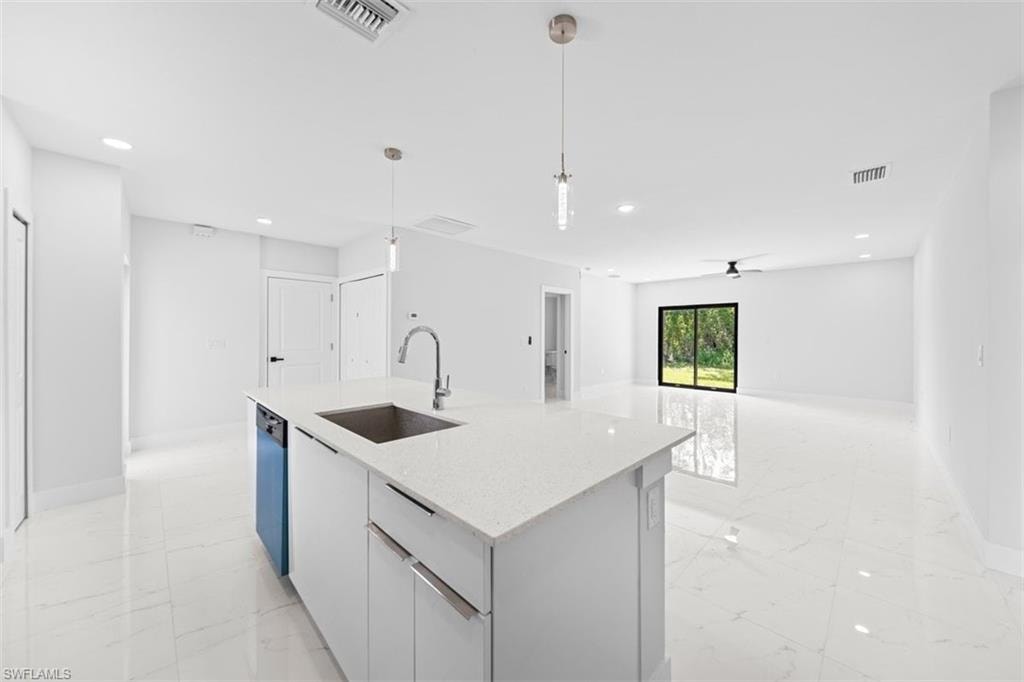 Modern kitchen featuring a large waterfall-edge island with white quartz countertops, stainless steel undermount sink with gooseneck faucet, white shaker-style cabinetry, polished porcelain flooring, recessed and pendant lighting, and abundant natural light from expansive windows